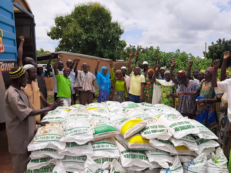 A group of farmers stands around a pallet of seed or fertilizer bags