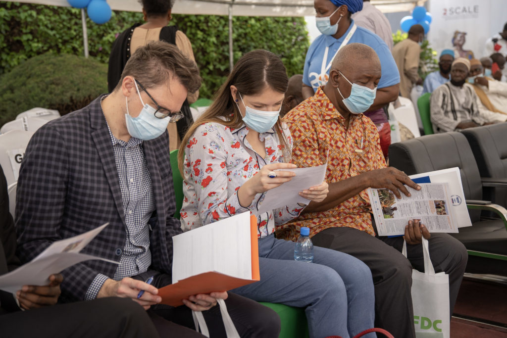 Two men and a woman sit in chairs reading printed pamphlets about IFDC.