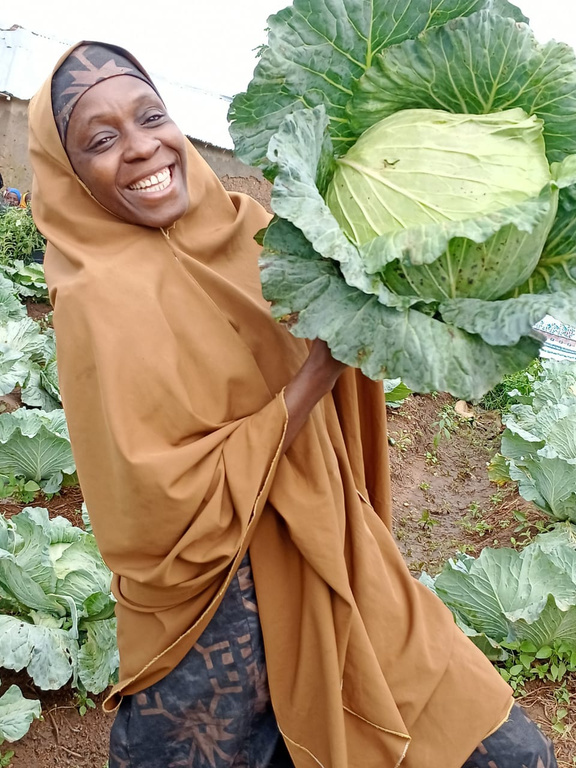 Saudatu Yakubu, a female smallholder farmer from Nigeria, holds a head of cabbage in her field.