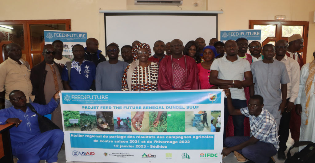 Over 25 participants from the workshop pose with an event banner; two men are kneeling to hold the banner in front of the standing group.