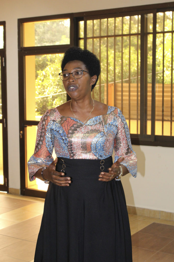 A woman in a multi-colored top gives a speech in front of a window