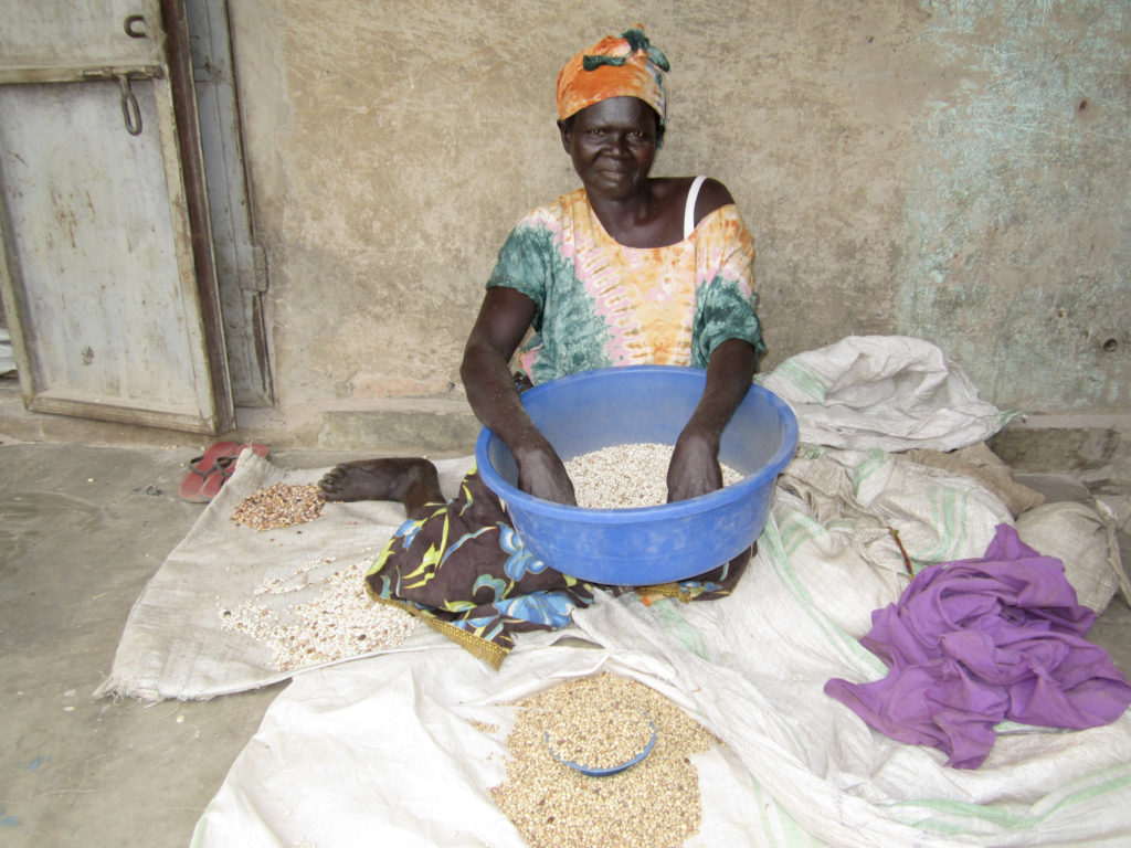 A woman sits on blankets on the ground holding a blue bowl of grain