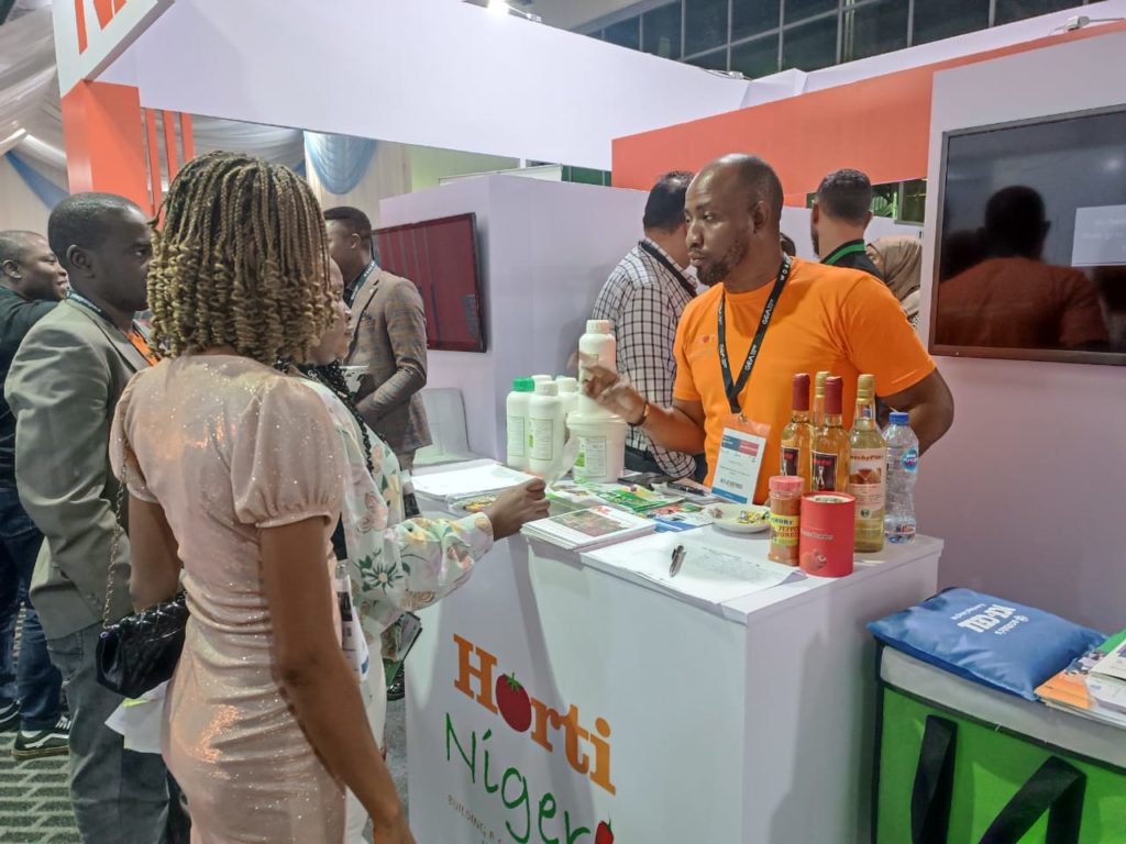 A women in a light colored dress speaks to a man at the HortiNigeria booth