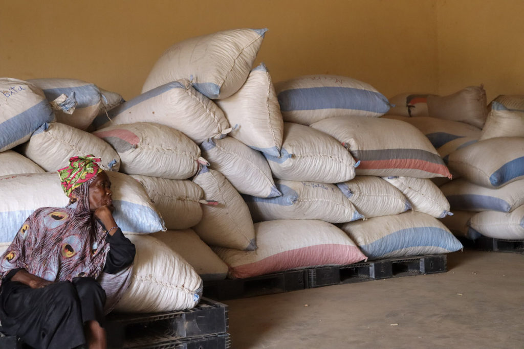 A woman sits in front of bags of fertilizer that are stacked against a wall