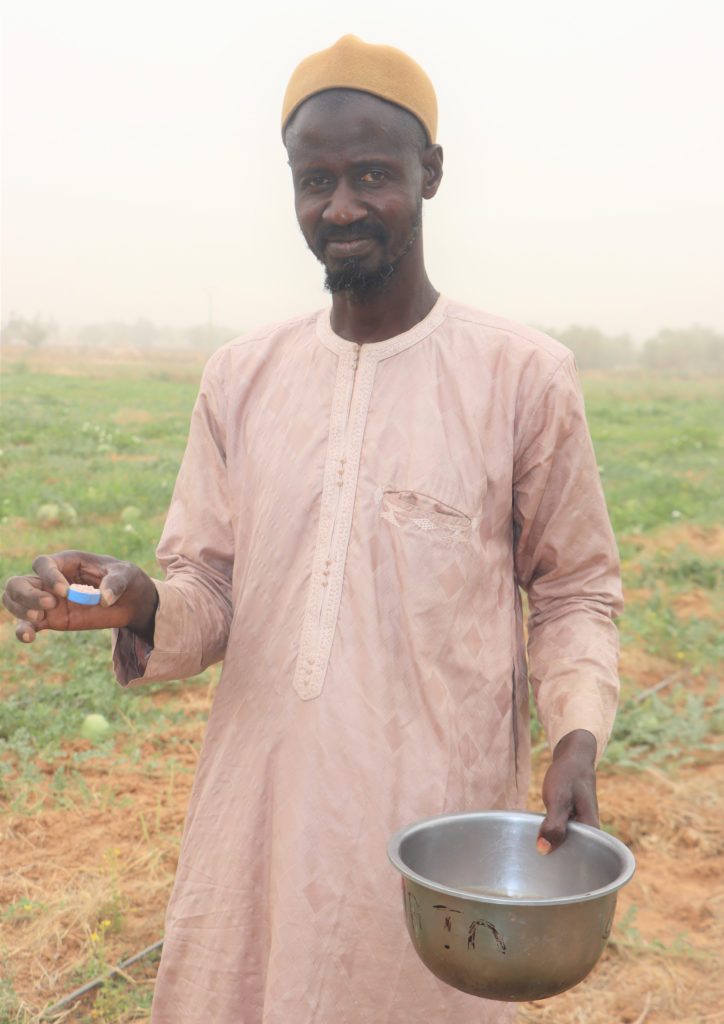 A man wearing pink holds a cap-full of fertilizer and a silver bowl