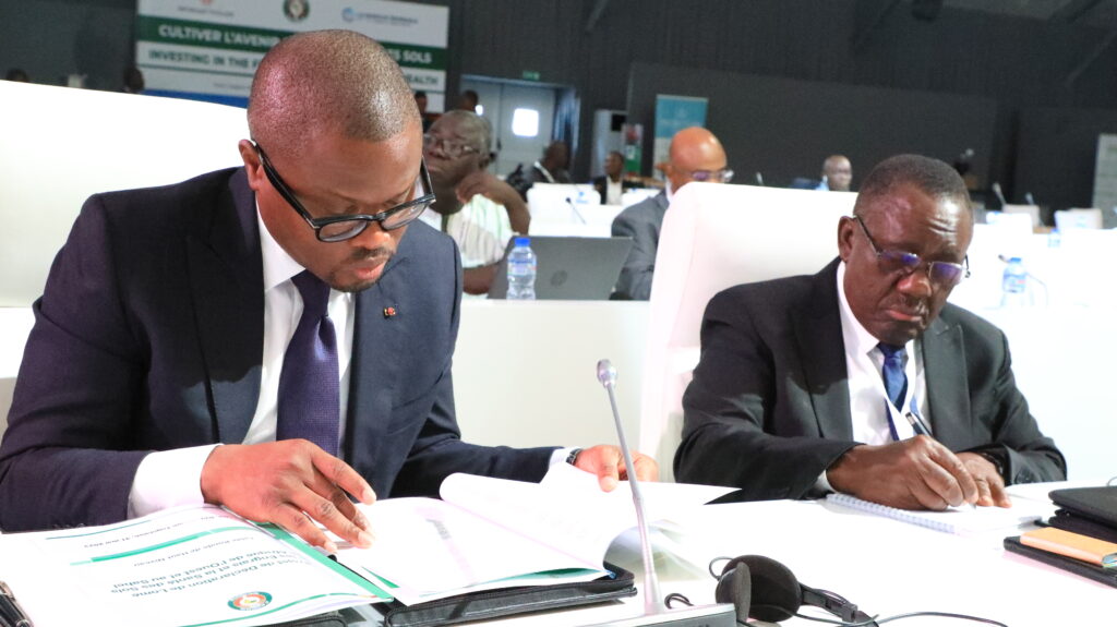 two men in suits look at documents on a table