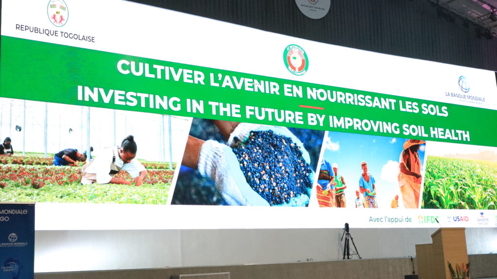 A screen that says, "Investing in the future by improving soil health" in both French and English