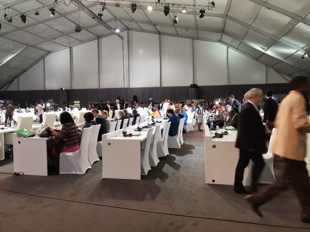 A large room with people sitting at tables, standing, walking