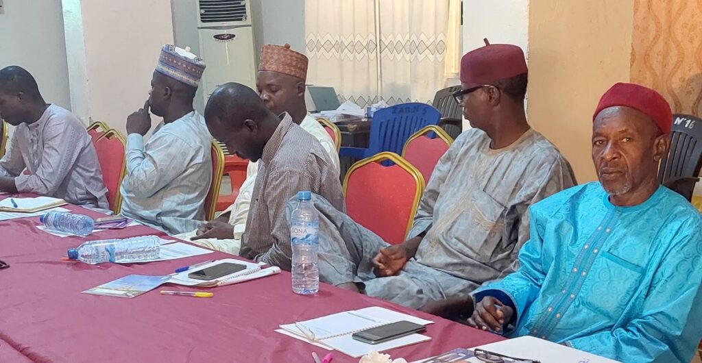 A group of men sitting at the right side of the table and looking to their left as someone is speaking out of frame. 