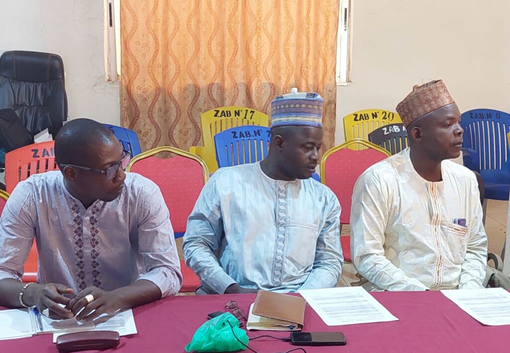 Three men sitting at a table on the same side looking to their right.