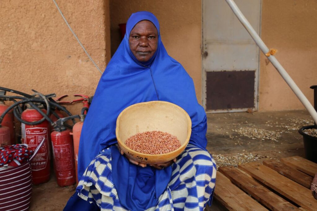 A woman dressed in blue clothes showing her seeds in a bowl.
