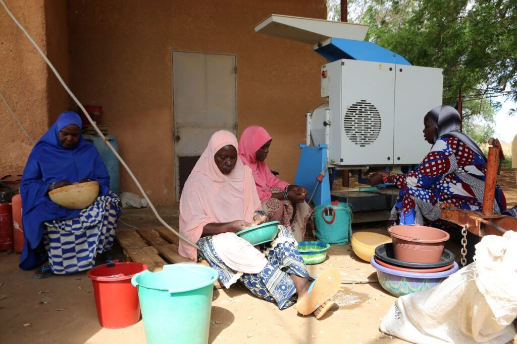 A group of women sitting down with bowls of seeds and working together. 