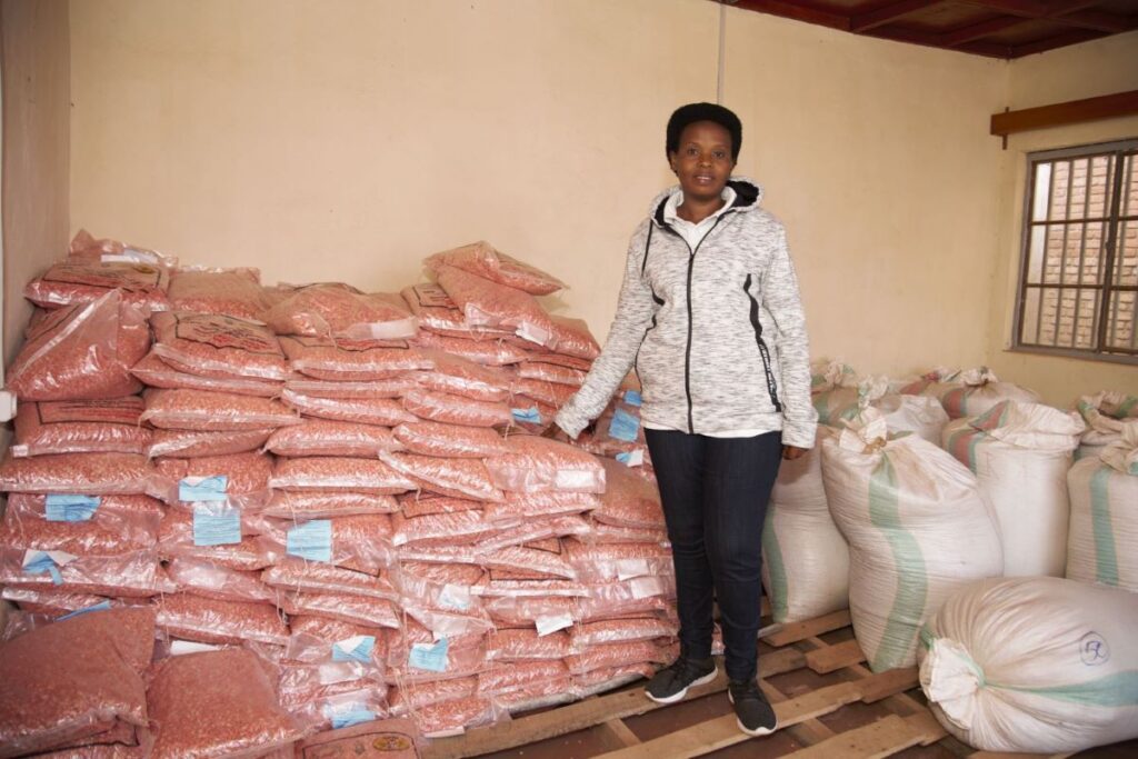 Anitha Nahimana is posed next to a structured pile of bags of seeds.