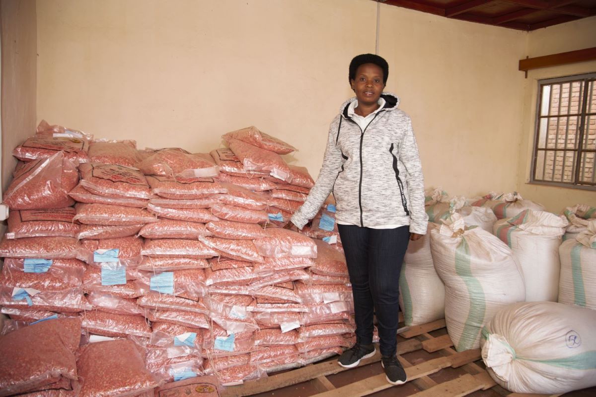 Anitha Nahimana is posed next to a structured pile of bags of seeds.