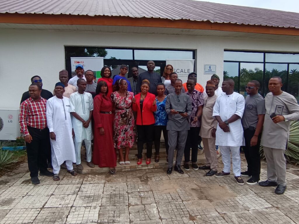 A group of people posing and smiling in front of 2SCALE and HortiNigeria posters.