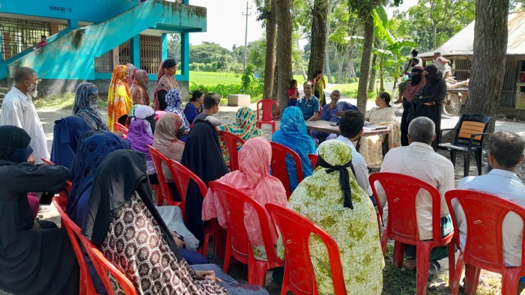 The delegation in front of a group of farmers sitting down and having a meeting outside. 