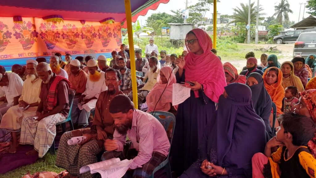 A female farmer standing up to give insights at a meeting with other local farmers. 