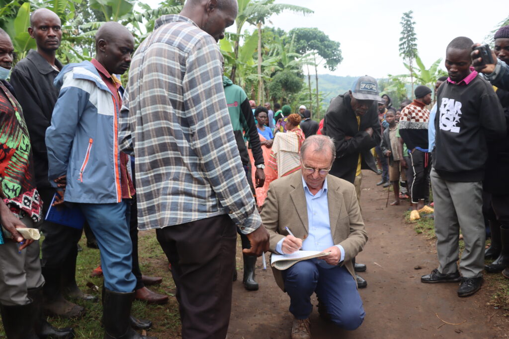 A man signs a piece of paper surrounded by a group of people