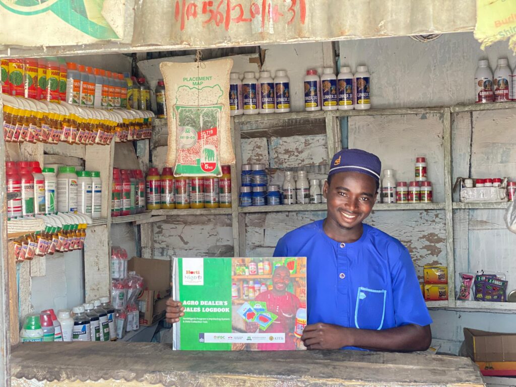 A young agripreneur at an agro input store holding the HortiNigeria Agrodealer Sales Logbook.