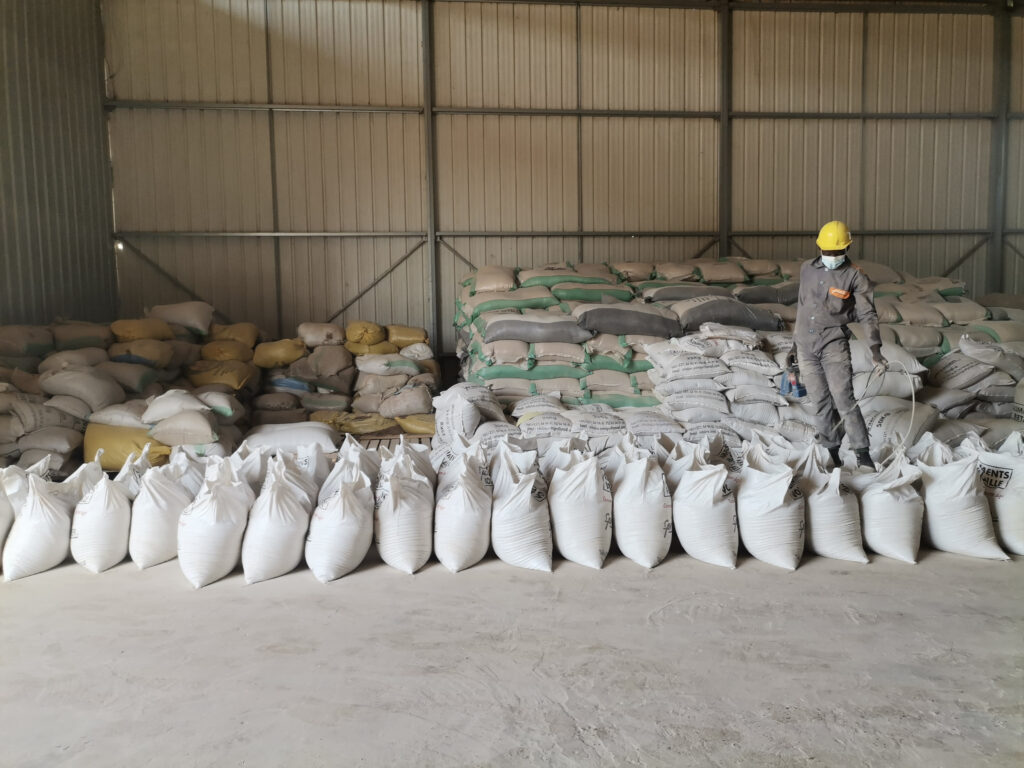 A staff worker stands by a group of aligned fertilizer bags in a warehouse.